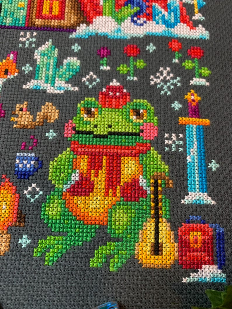 May include: A green frog wearing a red scarf and a red hat is holding a yellow guitar. The frog is sitting on a gray background with snowflakes and other winter-themed designs.