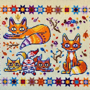 Puede incluir: Un patr&oacute;n de punto de cruz con cinco zorros naranjas con detalles blancos. Los zorros est&aacute;n rodeados por un borde de estrellas y cuadrados coloridos.