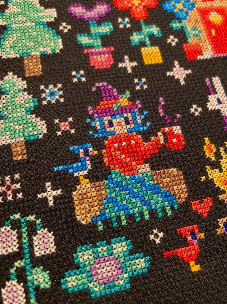 May include: A colorful cross-stitch pattern featuring a whimsical character wearing a hat and holding a cup, surrounded by trees, flowers, and other small details.