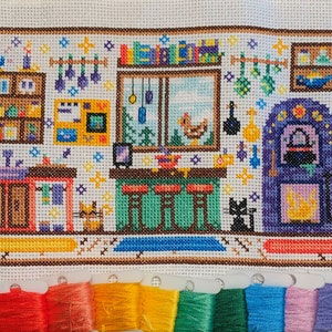 May include: Cross-stitch pattern of a kitchen with a fireplace, shelves, a window, and a cat. The kitchen is decorated with a variety of items, including a broom, a cauldron, and a chicken. The colors used in the pattern are mostly brown, yellow, green, and purple.