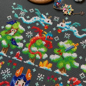 May include: A cross-stitch pattern featuring a winter wonderland scene with a red dragon, a green tree, a blue and orange character, and a white snowman. The pattern is on a dark gray fabric with white snowflakes.