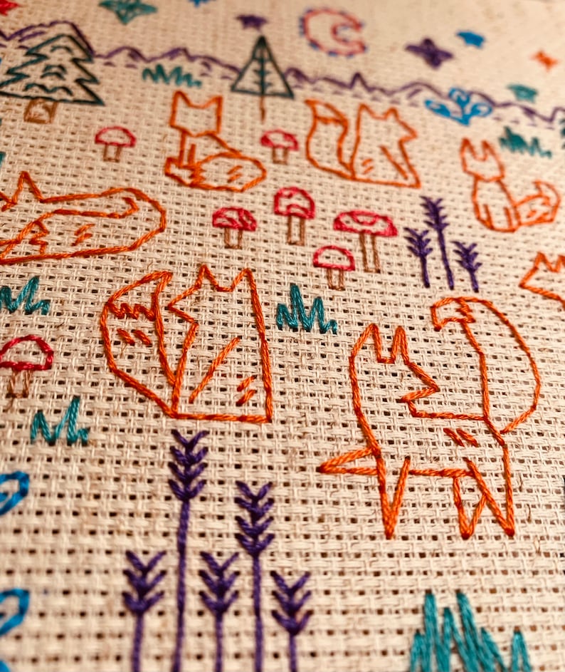May include: Embroidered design on a beige fabric featuring multiple orange foxes, green trees, purple flowers, and red mushrooms.