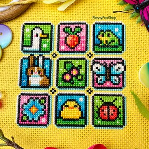 May include: A cross-stitch pattern with nine colorful squares featuring various spring-themed images, including a duck, a strawberry, a frog, a bunny, a flower, a butterfly, a chick, a ladybug, and a flower. The pattern is on a yellow background with the text "FlossyFoxShop" in the top right corner.