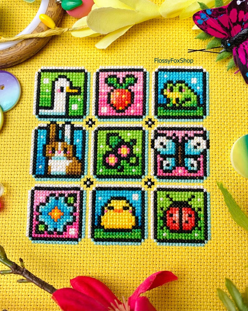 May include: A cross-stitch pattern with nine colorful squares featuring various spring-themed images, including a duck, a strawberry, a frog, a bunny, a flower, a butterfly, a chick, a ladybug, and a flower. The pattern is on a yellow background with the text "FlossyFoxShop" in the top right corner.