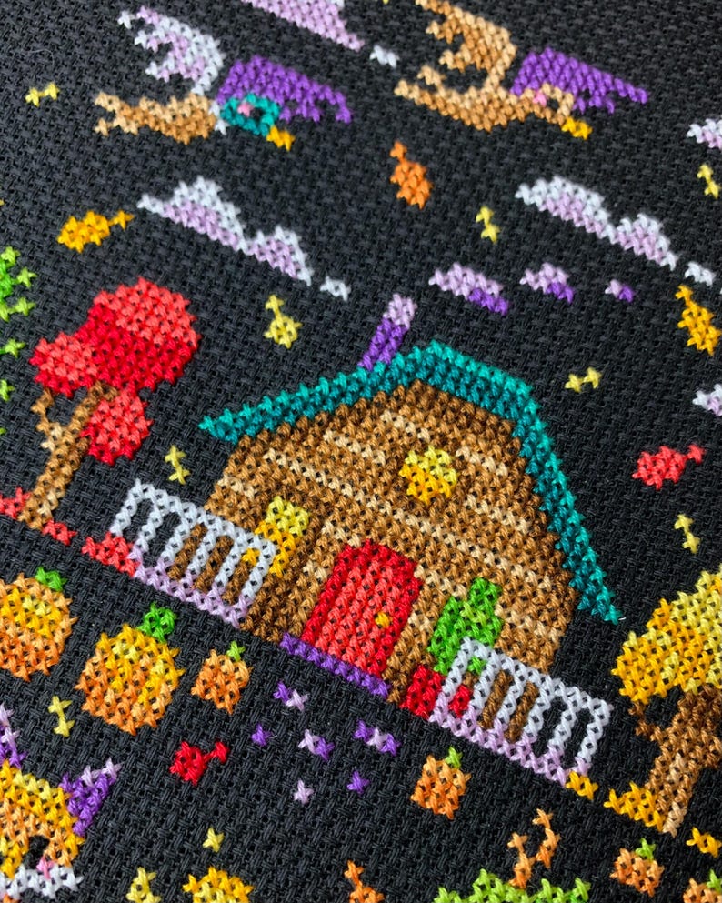 May include: A cross-stitch design featuring a whimsical Halloween scene. A brown house with a teal roof and red door is surrounded by pumpkins, trees, and flying witches against a black background. The design uses various colors to create a festive atmosphere.
