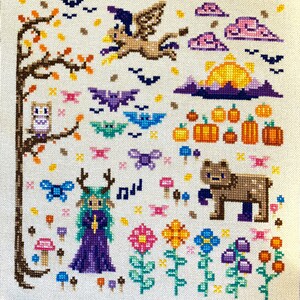 May include: Cross-stitch embroidery featuring a whimsical autumn scene with a purple-clad fairy, a brown bear, a flying bird, and a variety of mushrooms, flowers, and bats.