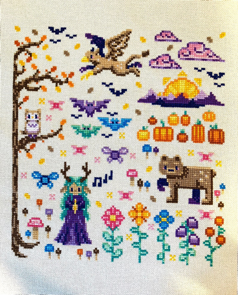 May include: Cross-stitch embroidery featuring a whimsical autumn scene with a purple-clad fairy, a brown bear, a flying bird, and a variety of mushrooms, flowers, and bats.