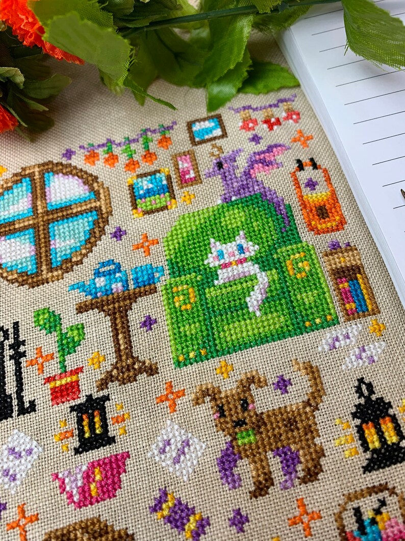 K&ouml;nnte beinhalten: Ein Kreuzstichmuster mit einer fantasievollen Szene mit einer Katze, einem Hund, einem Drachen, einem Fenster und anderen kleinen Details. Das Muster ist auf einem beigefarbenen Stoff mit bunten F&auml;den gestickt.
