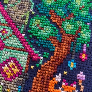 May include: Cross-stitch embroidery on dark blue fabric. The design features a tree with green leaves and a brown trunk, a fox, and floral and star accents. The colour palette includes shades of green, brown, orange, pink, and blue.