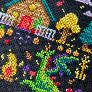 May include: Cross-stitch design featuring a whimsical scene with a house, trees, and a dragon. The house has a brown roof and a red door. A green dragon with purple wings is in the foreground. The background is black, with colorful accents.