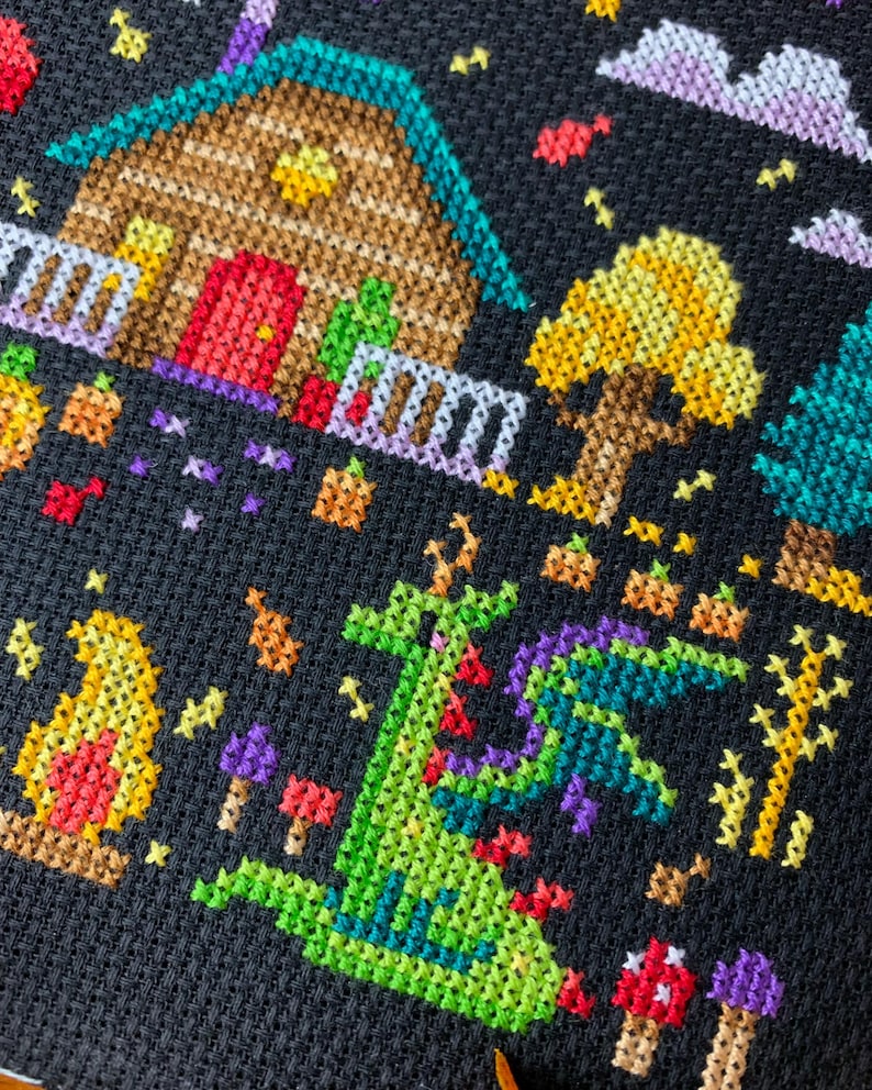 May include: Cross-stitch design featuring a whimsical scene with a house, trees, and a dragon. The house has a brown roof and a red door. A green dragon with purple wings is in the foreground. The background is black, with colorful accents.