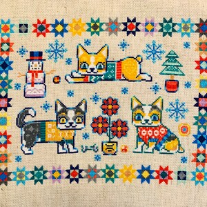 Peut inclure: Motif de point de croix repr&eacute;sentant quatre chats portant des pulls et un bonhomme de neige. L'arri&egrave;re-plan est une bordure color&eacute;e d'&eacute;toiles et de flocons de neige.
