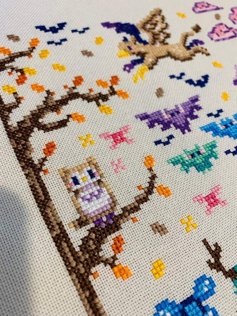 May include: Cross-stitch pattern featuring a brown owl perched on a branch with orange and yellow leaves. The owl is wearing a purple and white dress. There are bats and other flying creatures in the background.