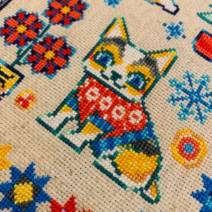 Peut inclure: Motif de point de croix repr&eacute;sentant un chat mignon portant une &eacute;charpe rouge et bleue avec le mot "COOO" dessus. Le chat est entour&eacute; de fleurs, de flocons de neige et d'autres motifs g&eacute;om&eacute;triques.