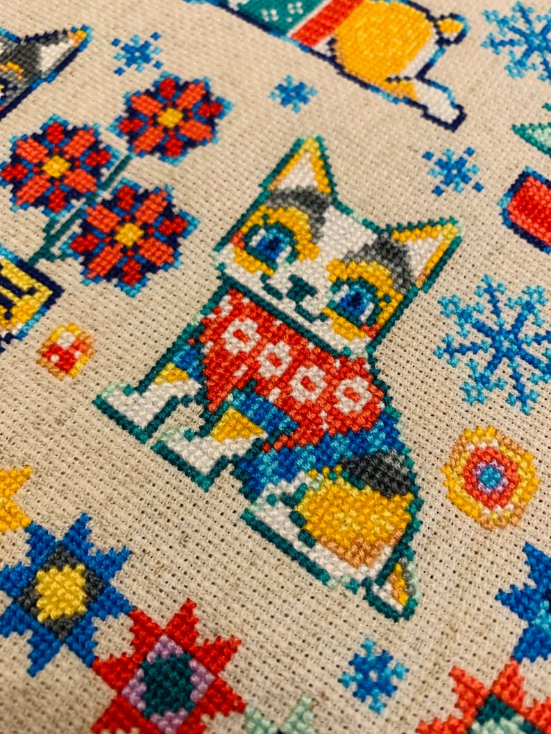 Peut inclure: Motif de point de croix repr&eacute;sentant un chat mignon portant une &eacute;charpe rouge et bleue avec le mot "COOO" dessus. Le chat est entour&eacute; de fleurs, de flocons de neige et d'autres motifs g&eacute;om&eacute;triques.