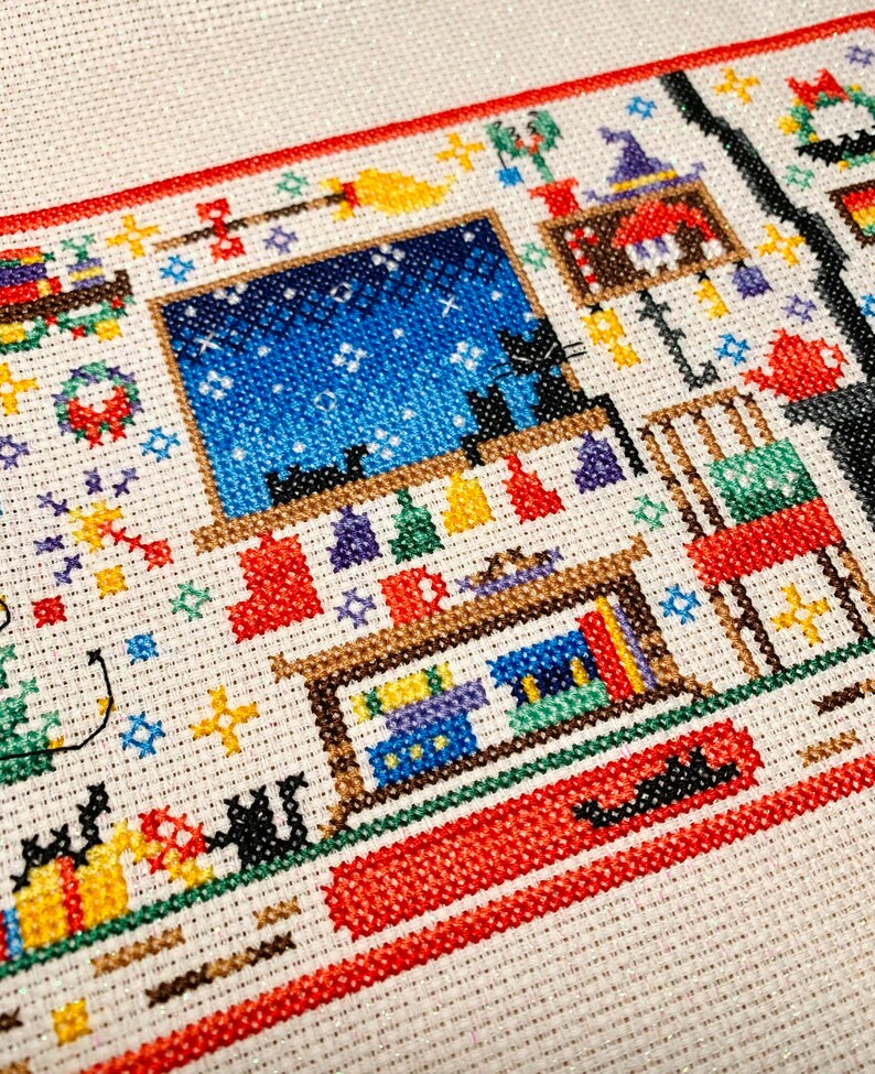 Puede incluir: Patr&oacute;n de punto de cruz de una habitaci&oacute;n con una ventana que muestra un cielo nocturno estrellado, una estanter&iacute;a con libros y un gato sentado en un alf&eacute;izar de la ventana. La habitaci&oacute;n est&aacute; decorada con una corona, una escoba y un sombrero de bruja.