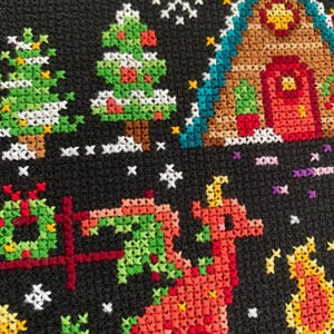 May include: A cross-stitch pattern featuring a red dragon, a green Christmas tree, a gingerbread house, and a yellow star on a black background.