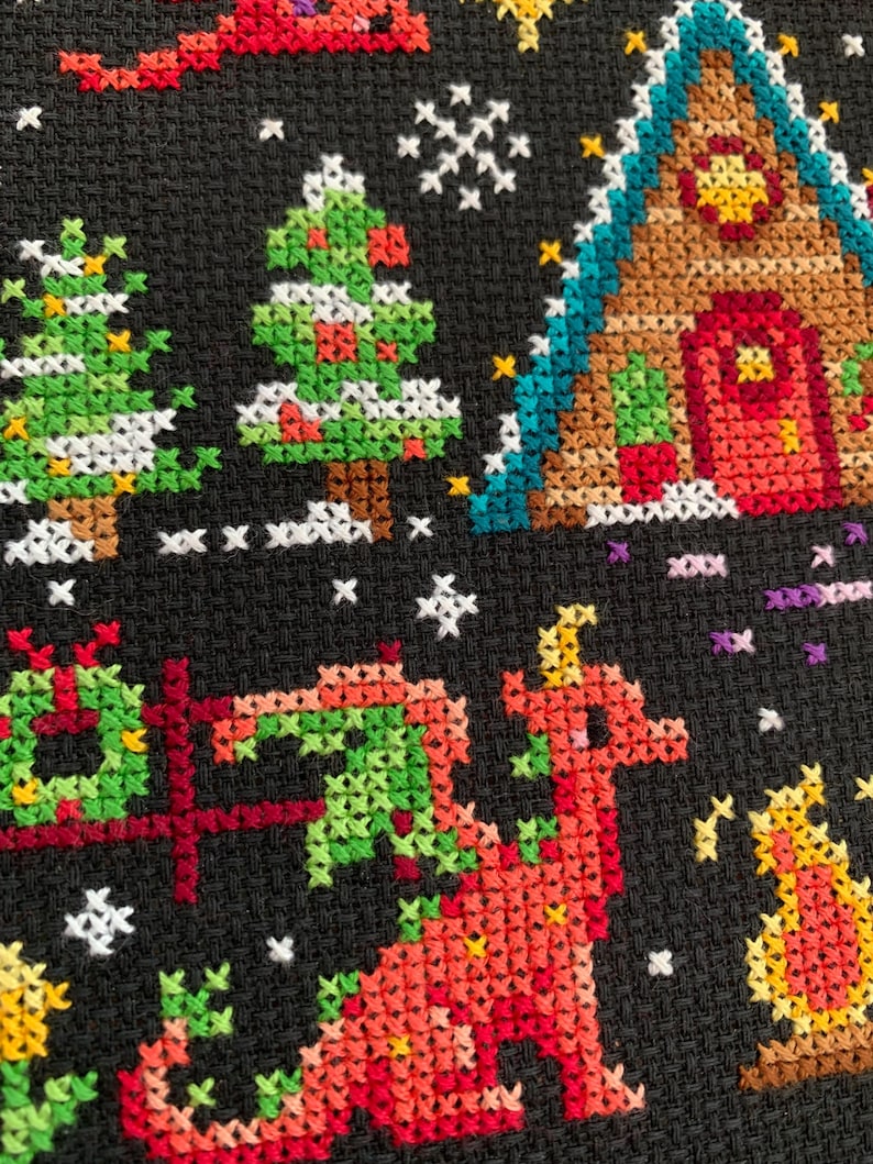 May include: A cross-stitch pattern featuring a red dragon, a green Christmas tree, a gingerbread house, and a yellow star on a black background.