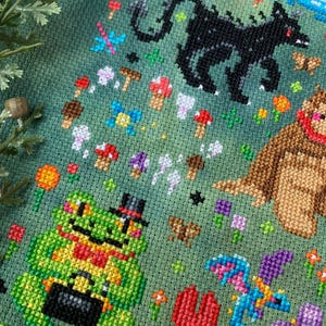May include: A green cross-stitch embroidery featuring a variety of whimsical creatures, including a frog wearing a top hat, a dragon, a bear, and a black monster. The background is a green field with flowers and mushrooms.
