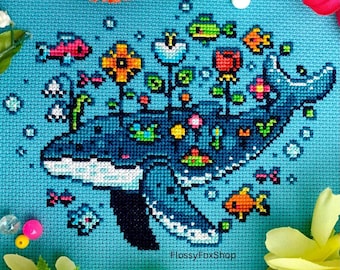 May include: Cross-stitch art featuring a blue whale with flowers and fish. The whale is in shades of blue, with white accents. Colorful flowers and fish are scattered around the whale on a light blue background. The text "FlossyFoxShop" is in the bottom right corner.
