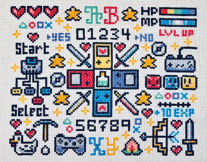 Peut inclure: Broderie au point de croix repr&eacute;sentant des &eacute;l&eacute;ments de jeux vid&eacute;o r&eacute;tro. Elle comprend des c&oelig;urs, des &eacute;toiles, des &eacute;p&eacute;es, des manettes et du texte comme "Start" et des chiffres. La palette de couleurs est vive, avec du rouge, du bleu, du jaune et du vert.
