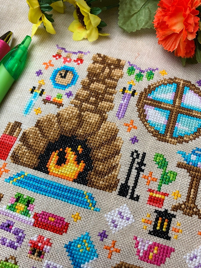 K&ouml;nnte beinhalten: Ein Kreuzstichmuster mit einem gem&uuml;tlichen Kamin mit einem knisternden Feuer, einem Fenster mit einem blauen und wei&szlig;en Bleiglasfenster und verschiedenen anderen Details wie einer Uhr, einem Schwert und einer Topfpflanze. Das Muster ist auf einem beigefarbenen Stoff gestickt.