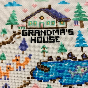 Puede incluir: Bordado de punto de cruz de una casa con el texto "Grandma's House" y un lago con el texto "Lake". La escena incluye &aacute;rboles, nubes, corazones y zorros.