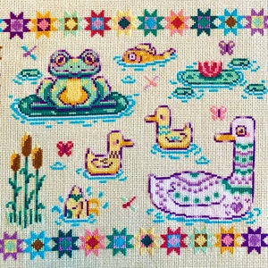 May include: A cross-stitch embroidery design featuring a frog sitting on a lily pad, a duck, a swan, and a variety of flowers and plants. The design is surrounded by a border of colorful stars.