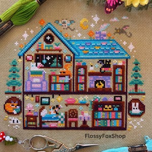 May include: A cross-stitch pattern of a whimsical two-story house with a blue roof and colorful details. The design includes bookshelves, a fireplace, and various decorative elements. The text "FlossyFoxShop" is visible.