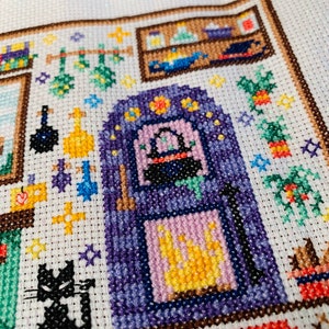 May include: A cross-stitch pattern of a witch's kitchen with a black cat, a cauldron, and a variety of herbs and potions.