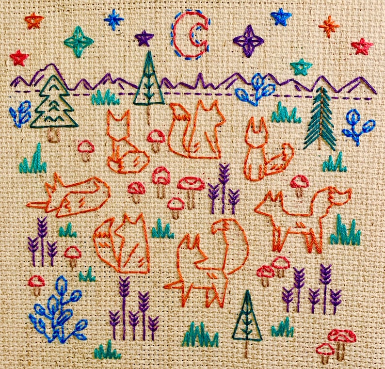 May include: Embroidered design on a beige fabric featuring a moon, stars, trees, and foxes. The foxes are orange and brown with white accents. The design is surrounded by a border of green and blue.