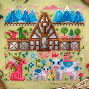 May include: Cross-stitch embroidery featuring a whimsical scene with a brown house, blue mountains, and pink clouds. A pink dragon and a cow with blue spots are in the foreground, surrounded by flowers. The text "FlossyFoxShop" is visible.