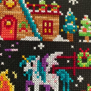 May include: Cross-stitch pattern of a winter scene with a unicorn, a gingerbread house, and Christmas trees. The unicorn is white with a purple mane and tail, and it is standing in front of a red fence. The gingerbread house is brown with a red door and white trim. The Christmas trees are green with white lights and red ornaments.