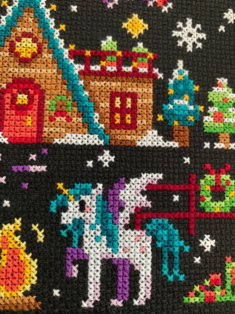 May include: Cross-stitch pattern of a winter scene with a unicorn, a gingerbread house, and Christmas trees. The unicorn is white with a purple mane and tail, and it is standing in front of a red fence. The gingerbread house is brown with a red door and white trim. The Christmas trees are green with white lights and red ornaments.