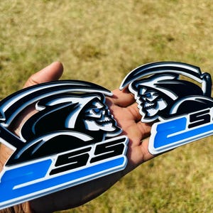 May include: Two black and white 3D printed car emblems with a grim reaper design and the text "2SS" in blue and white.