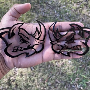 May include: Two black vinyl decals of a rhinoceros head with an angry expression. The decals are cut out and have a detailed design.