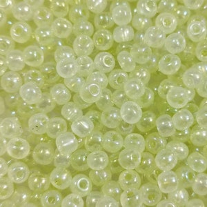 May include: A close-up image of a large quantity of small, round, translucent, light green beads. The beads have a slight iridescent sheen.