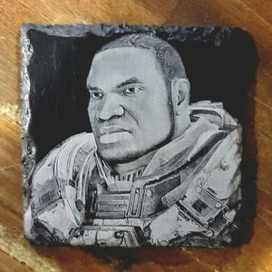 Puede incluir: Una baldosa cuadrada de pizarra grabada en negro y gris con un retrato de un hombre con vestimenta de estilo militar. La imagen es una representación detallada en escala de grises, que muestra el rostro y el uniforme del hombre. La baldosa tiene un borde rugoso y natural.