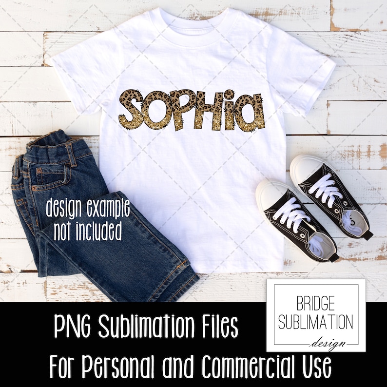 May include: A white t-shirt with the name "SOPHIA" printed in gold glitter letters with a leopard print pattern. The shirt is on a white wooden background with blue jeans and black sneakers.