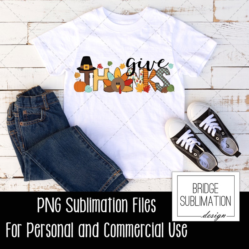 May include: White t-shirt with the words "give thanks" in a colorful Thanksgiving-themed design. The design includes a turkey, a pilgrim hat, and fall leaves. The image also shows a pair of blue jeans and black sneakers.