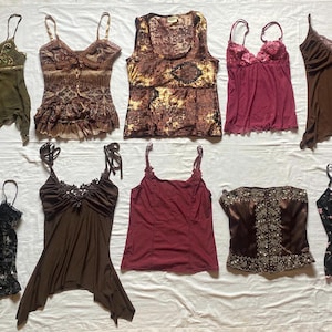 Può includere: Una collezione di dieci top senza maniche disposti su due file. L'assortimento comprende varie canotte e camisole in tonalità verde oliva, marrone, bordeaux, nero e rosa, con dettagli come bordi in pizzo, paillettes e stampe floreali.