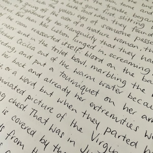 Puede incluir: Primer plano de un texto escrito a mano en una hoja de papel blanca. El texto describe una escena de una mujer en un ba&ntilde;o, con detalles sobre sus lesiones y los eventos que llevaron a ellas. El texto menciona un torniquete, sangre y un lavabo con una navaja.