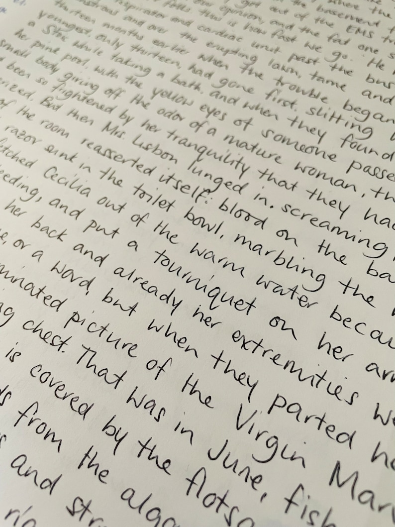 Puede incluir: Primer plano de un texto escrito a mano en una hoja de papel blanca. El texto describe una escena de una mujer en un ba&ntilde;o, con detalles sobre sus lesiones y los eventos que llevaron a ellas. El texto menciona un torniquete, sangre y un lavabo con una navaja.