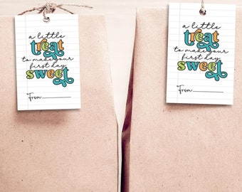 May include: Two brown paper bags with white gift tags attached. The tags have a handwritten message that reads "a little treat to make your first day sweet" with a colorful illustration of the word "treat".