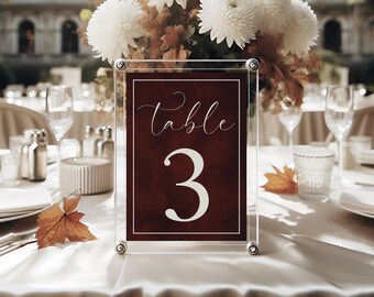 May include: A clear acrylic table number holder with a burgundy card that says "Table 3" in white script font. The card has a subtle watercolor effect.
