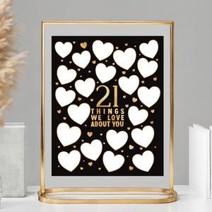 Puede incluir: Un cartel negro y blanco con marco dorado con 21 formas de corazón en blanco. El cartel dice "21 cosas que amamos de ti".