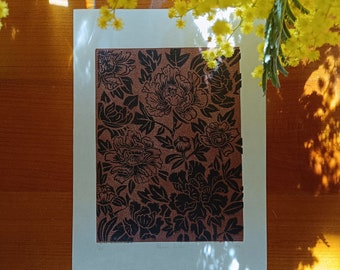 May include: A floral print art piece featuring a brown background with black peony flowers. The artwork is set within a white border, with yellow flowers in the upper portion of the image. The artwork is displayed on a wooden surface.