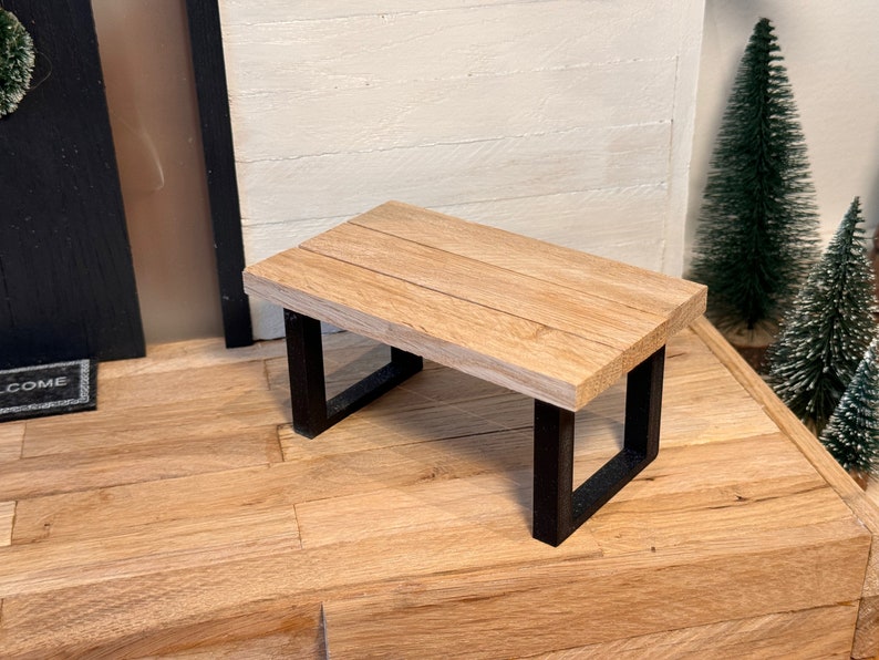 Peut inclure: Un petit banc en bois avec des pieds en m&eacute;tal noir. Le banc est en bois clair et a une finition naturelle. Les pieds sont carr&eacute;s et ont une finition noire en poudre.