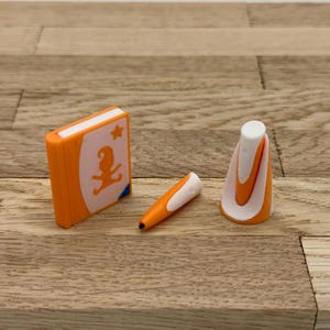Könnte beinhalten: Ein orangefarbenes und weißes Buch mit einem Stern und einer Comicfigur auf dem Cover, ein orangefarbener und weißer Stift und ein orangefarbener und weißer Kegel.