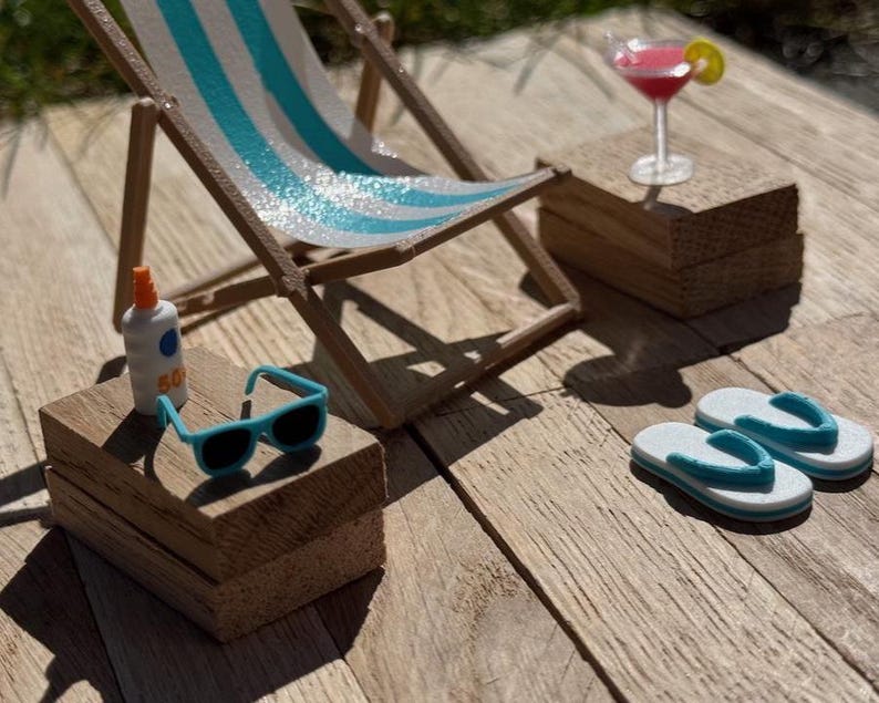 May include: A miniature beach scene with a striped deck chair, sunglasses, sunscreen, a cocktail, and flip-flops. The chair has blue and white stripes. The sunglasses are turquoise. The cocktail has a lemon slice. The scene is set on a wooden surface.